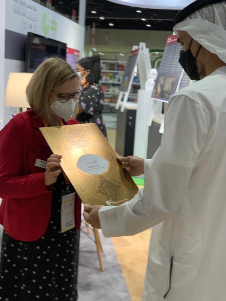 Fr. Claudia Kaiser, Vizepräsidentin der Frankfurter Buchmesse überreicht feierlich eine edle goldene Mappe an den Sohn des Kronprinzen